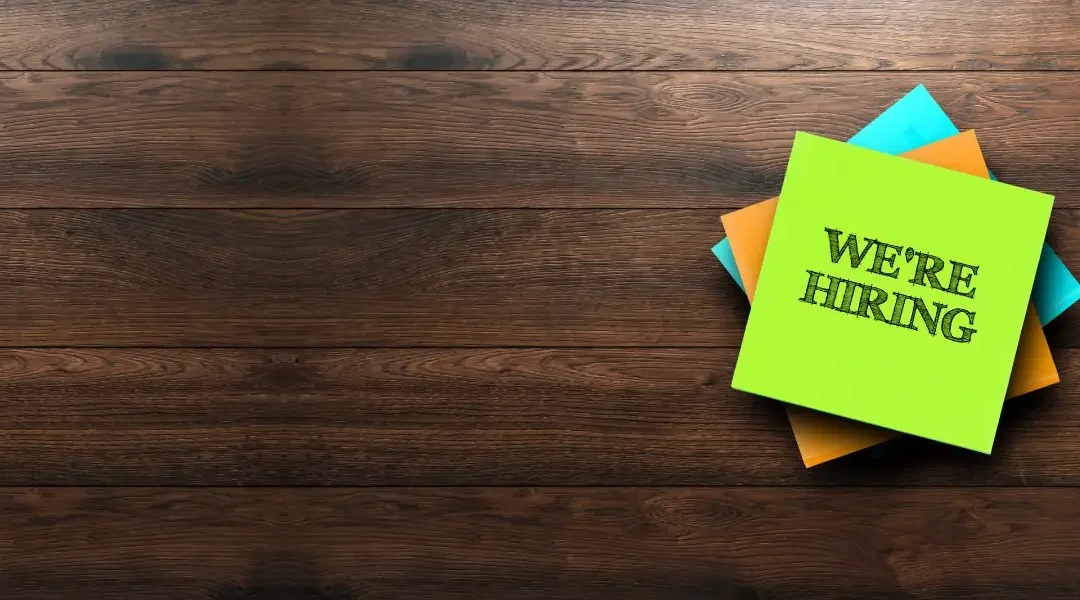 A pile of post-it notes on a table with the top saying "We're Hiring"
