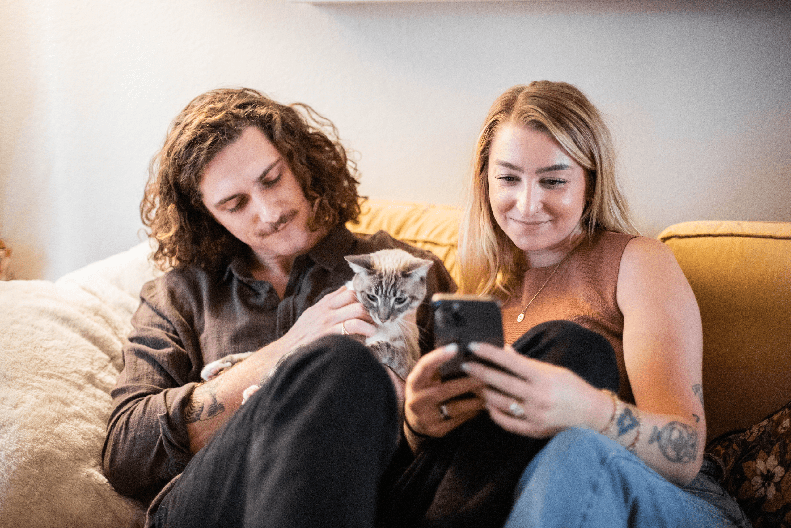 Pet parents sitting together with cat while looking at their phone Pet parents sitting together with cat while looking at their phone