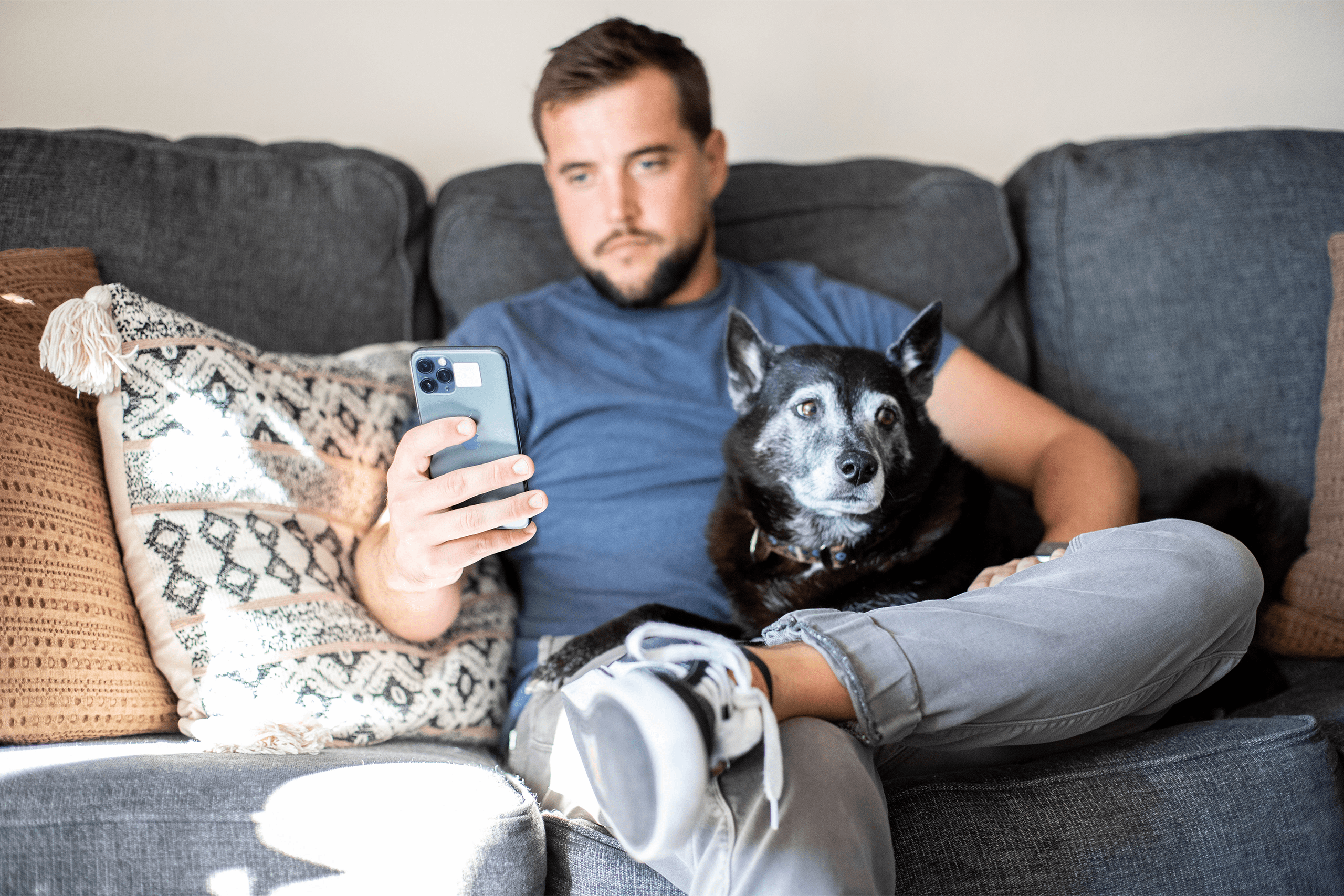Quick access to pet records_PetDesk Pet parent using mobile app while sitting on the couch with his dog